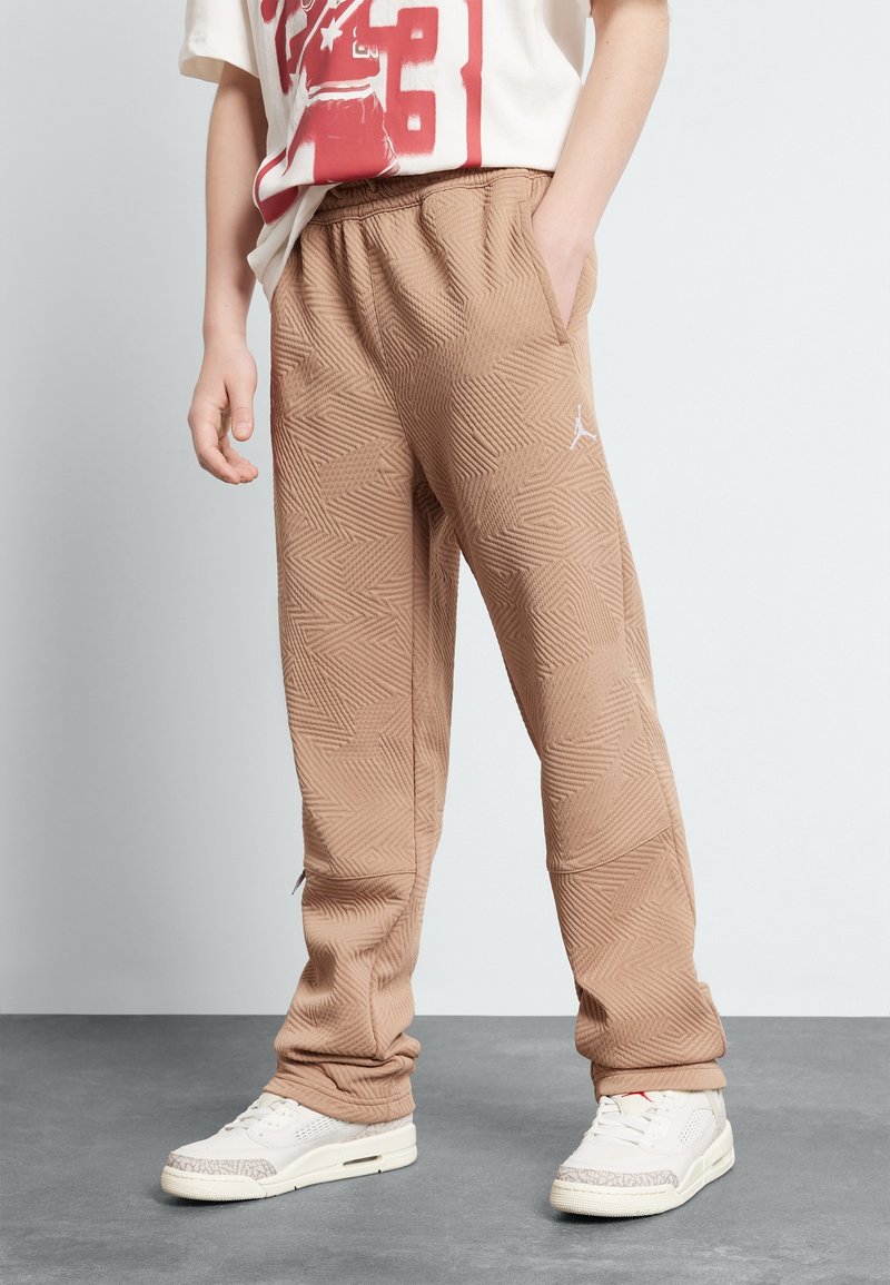 Ljust bruna mönstrade joggerbyxor med elastisk midja och fickor, kombinerade med vita sneakers med grå accenter.