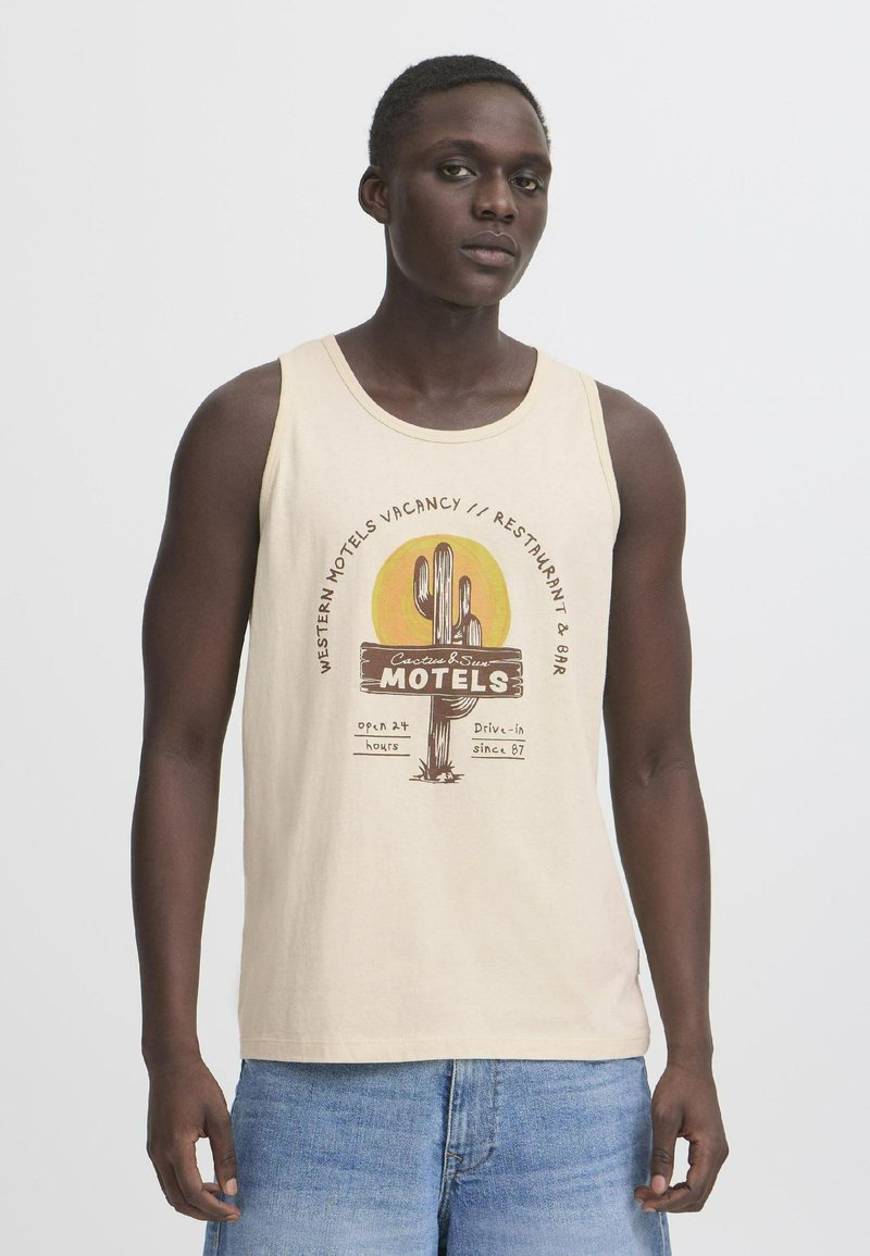 Camiseta sin mangas beige con un estampado gráfico de un cactus y un letrero de motel con el texto "Motel Western Vacante". La tela parece suave y transpirable.