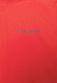 Surface en tissu rouge avec le nom de la marque "DIDRIKSONS" imprimé en gris foncé au centre.