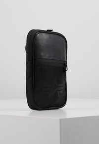 Svart zippered väska med en slät läderfront och en meshpanel med en logotyp. Tunn och rektangulär form, designad för kompakt förvaring.
