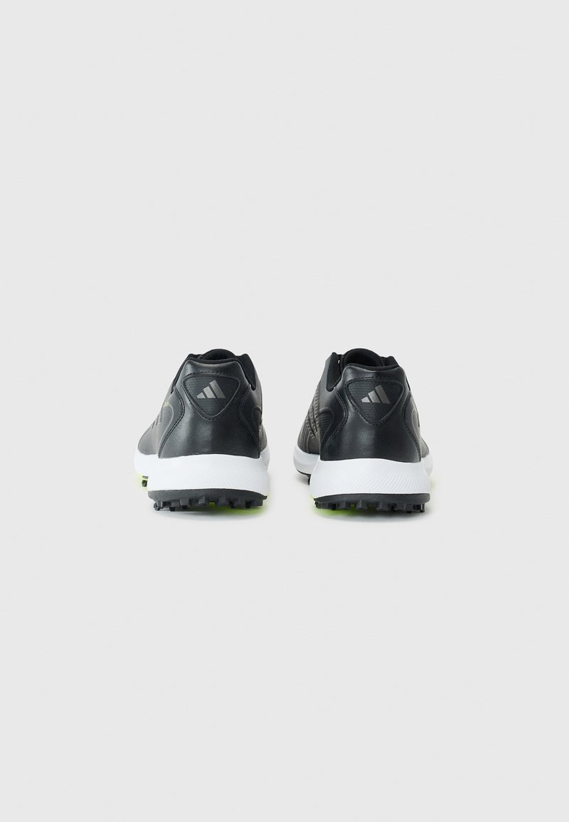 Schwarze Sportschuhe mit einem glatten Lederoberteil, strukturierten Akzenten und einer weißen Sohle, die an der Unterseite schwarze und grüne Nieten aufweist.