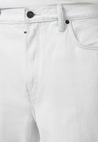 Hvide denimbukser med en glat tekstur, der har en knaplukning, sidelommer og kontrastsyninger.