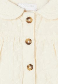 Kleid in Cremefarbe aus weichem, strukturiertem Stoff. Verfügt über einen runden Kragen, braune Vorderknöpfe und zarte Blumenstickerei.