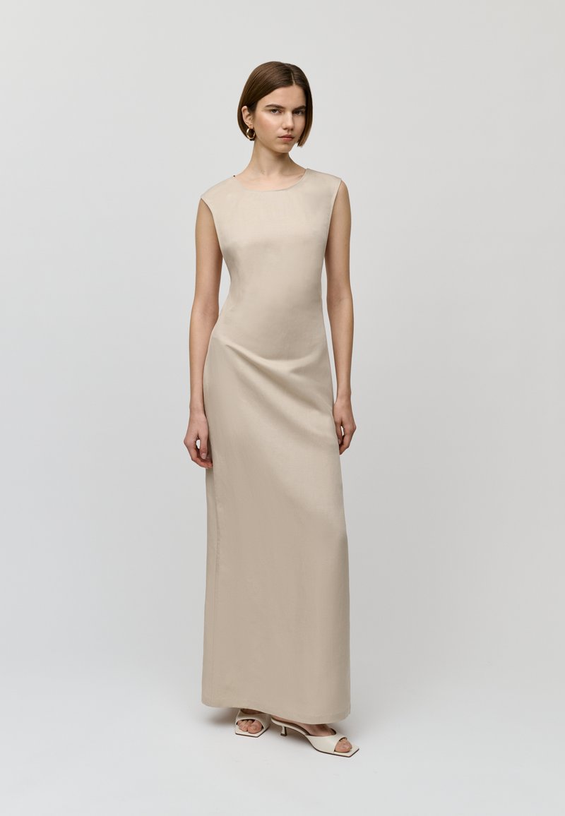 Abito lungo aderente in tessuto beige chiaro, caratterizzato da un design senza maniche e una texture liscia. Silhouette semplice ed elegante senza motivi visibili.
