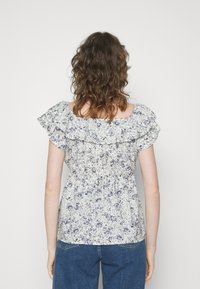 Blusa floral com mangas com babados, apresentando um tecido branco com padrões florais azuis; corpete ajustado com elástico franzido nas costas.
