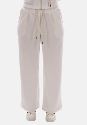Pantaloni morbidi di colore bianco sporco con pieghe anteriori, vita con coulisse, tasche laterali, orli risvoltati, indossati con sneaker bianche.