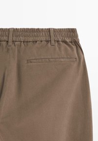 Bruine katoenen broek met een elastische tailleband, achterzak en een gladde textuur. Voorzien van riemlussen voor een verstelbare pasvorm en comfort.