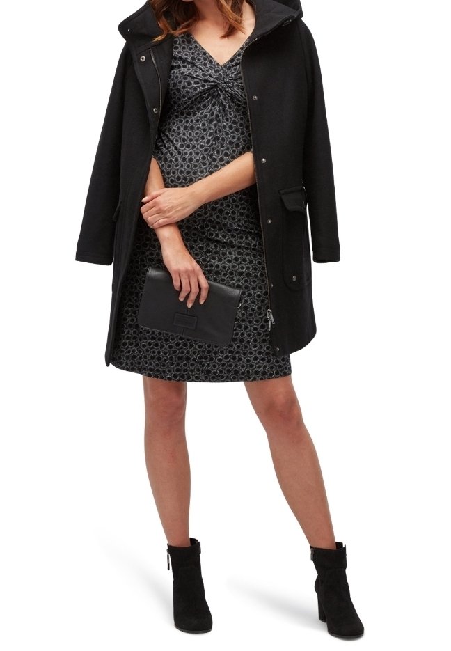 Zwarte overjas met capuchon, gedragen over een gemarmerde grijze jurk. De jurk heeft een verzamelde halslijn, gecombineerd met een zwarte clutch en enkelhoge laarzen.