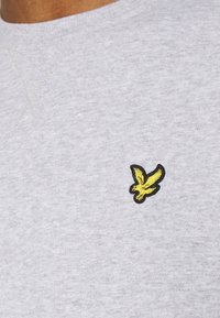 Gros plan sur une chemise grise avec un petit emblème d'oiseau jaune cousu sur la zone de la poitrine.