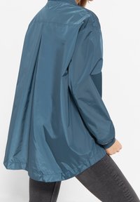 Dark blue, shiny, lightweight jacket with a loose fit, featuring a high collar, elastic cuffs, and a curved hemline.