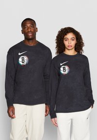 Nike majice dugih rukava u tamnosivoj boji s okruglim Brooklyn logom, sa klasičnim krojem, okruglim izrezom i mekanom pamučnom teksturom.