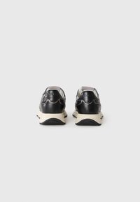 Een paar zwart-witte sneakers met dikke zolen, grijze hieltabs en de merknaam "PINKO" in reliëf op de achterkant.
