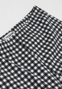 Černobílá tkanina s kostkovaným vzorem a elastickým pasem. Měkká textura s hladkým povrchem. Štítek nese nápis "TEZENIS."