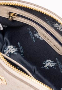 Pouch texturizado beige con un interior azul marino que presenta un patrón de logotipos repetido. El cierre dorado resalta la apertura, mejorando la practicidad.