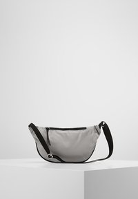 Szara torba z nylonu o zakrzywionym kształcie, czarny regulowany pasek oraz zamykana na zamek przednia kieszeń. Gładka tekstura i minimalistyczny design.