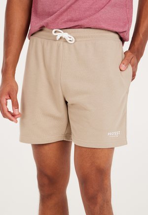 Beige shorts gemaakt van zachte stof met een elastische tailleband en een trekkoord. Heeft een logo in het wit gedrukt op de onderste linkerkant.