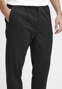 Pantalons taillés gris foncé avec une texture lisse, dotés d'un devant plat, de poches latérales et d'une coupe slim. Détail de taille ajustée.