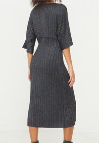 Knälång, mörk klänning med ribbad textur och metallisk lyster. Har ärmar som når till armbågen och en figurnära midja. Liten slits på sidan.