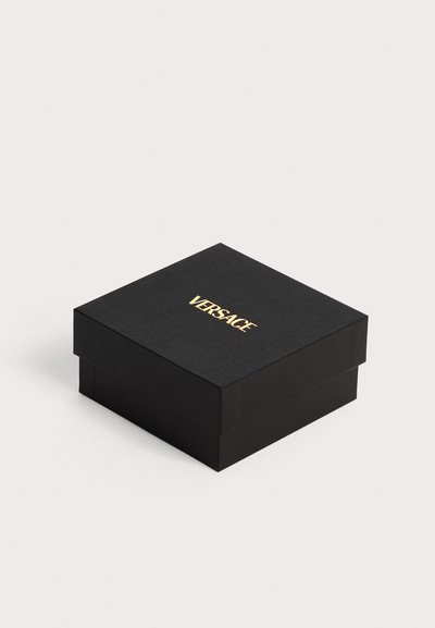 Boîte carrée noire texturée avec un couvercle, portant le mot « VERSACE » en lettres dorées centré sur le dessus.
