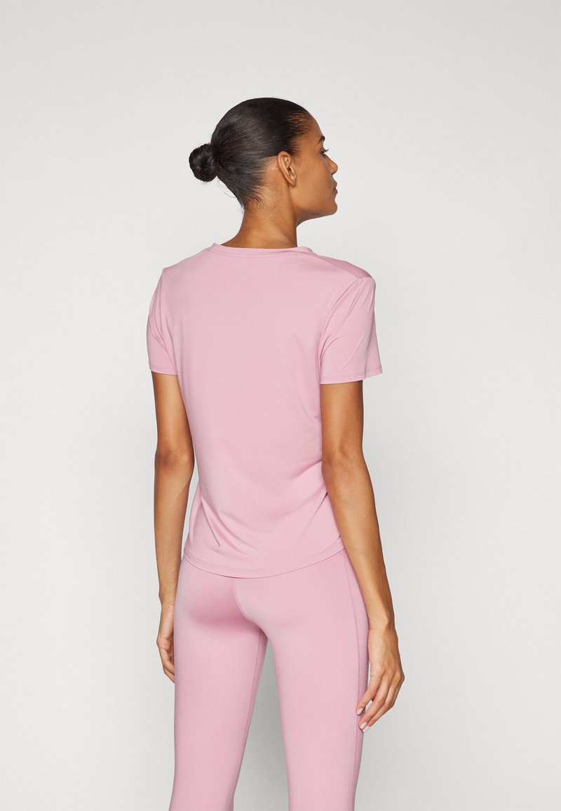 Kortärmad, figurnära topp i mjukt rosa tyg, med rund halsringning och slät yta, kombinerad med matchande rosa leggings.