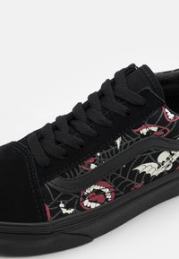 Baskets noires avec un tissu à motifs de chauves-souris et de crânes. Bout en daim, lacets noirs et semelle en caoutchouc texturée.