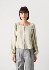 Lichtgroene, gemêleerde blouse met lange pofmouwen en een ronde halslijn, gesloten met knopen aan de voorkant, gecombineerd met grijs gestreepte broeken.