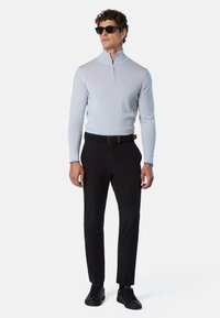 Maglione zip-up azzurro chiaro, pantaloni neri e sneakers nere. Texture liscia, design aderente. Gli occhiali da sole completano il look.