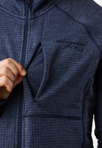 Donkerblauwe ritsjack met textuurstof. Voorzien van een borstzak met rits en het logo "SWEDENMOUNT" erboven.