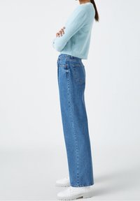 Suéter fuzzy azul claro, jeans rectos de cintura alta en azul, y zapatillas blancas con suela gruesa en una vista lateral.