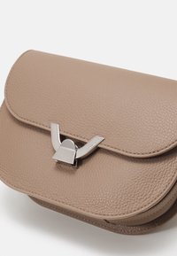 Struktureret læderhåndtaske i lys taupe med en tekstureret overflade, udstyret med en metallisk lukning og glatte kanter. Kompakt og rektangulært design.