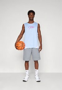 Světle modré tílko s růžovým potiskem, doplněné o šedé šortky. Model drží oranžový basketbalový míč a nosí bílé ponožky a boty.