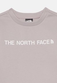 Gaiši pelēks īsām piedurknēm t-krekls no kokvilnas, ar baltu logo, kas uzdrukāts uz priekšas un lasāms kā "THE NORTH FACE".