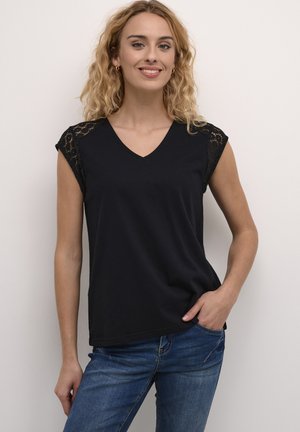 Black V-neck T-shirt with lace short sleeves, soft fabric, relaxed fit, paired with blue jeans. Model poses with one hand in pocket.