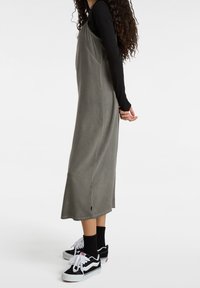 Vestido gris sin mangas con un dobladillo acampanado y una textura suave, superpuesto a una camiseta negra de manga larga. Combinado con zapatillas blancas y negras.