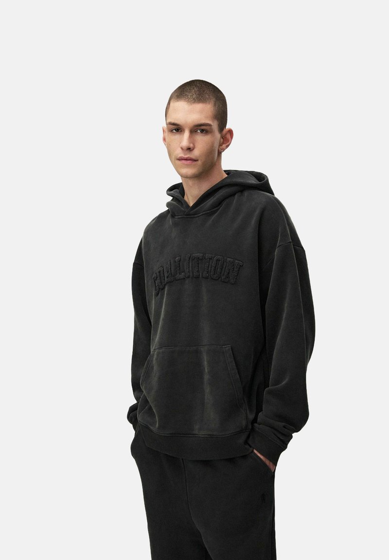 Czarna bawełniana bluza z kapturem z kieszenią kangurką i teksturowanym napisem "COALITION". Posiada luźny krój i sznurki w kapturze.
