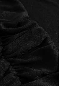 Melnas audums ar teksturētu ručingu un smalkām mirdzuma daļiņām. Materiāls šķiet maigs ar nelielu spīdumu, radot dinamisku virsmu.