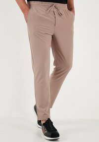Lichtbeige joggers gemaakt van zachte, rekbare stof, met een elastische tailleband, trekkoord en zijzakken. Draag ze met zwarte sneakers.