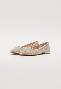 Scarpe flat con punta a punta, ricoperte di strass trasparenti su una base beige, con tacco basso e interno intrecciato.