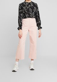 Blusa floreale nera con maniche a sbuffo, abbinata a pantaloni cropped rosa chiaro; modella che indossa sneakers bianche con accenti multicolori.