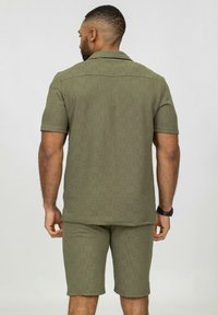 Chemise olive à manches courtes et shorts assortis, en tissu texturé, motif subtil, design décontracté avec col et coutures latérales.