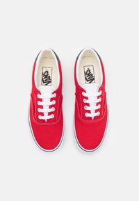 Sneakers di canvas rossi con lacci bianchi, dettagli neri sul tallone e suola in gomma. Presentano un logo sulla soletta e dettagli di cucitura.