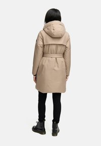 Beige, knælang puffers jakke med hætte, bælte i taljen og rygdetalje, sammen med sorte slim-fit bukser og sorte støvler.