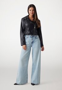 Black faux leather cropped jacket with silver zipper and snap, paired with light blue wide-leg jeans and black pointed-toe heels.