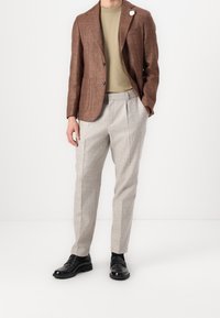 Brun texturerad blazer över en ljus olivfärgad t-shirt, tillsammans med ljusgrå rutiga byxor och svarta loafers. Inkluderar en vit slagaccent.