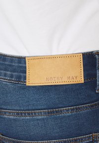 Modré džíny z denimu s hnědou koženou nášivkou značky "NOISY MAY", nošeny s vplněným bílým topem.