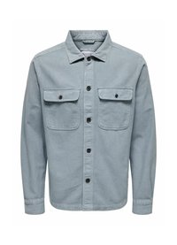 Camisa de mezclilla de color azul claro, con botones en negro, dos bolsillos en el pecho y un collar clásico. Textura suave y corte relajado.
