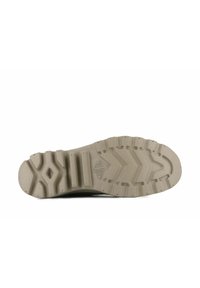 Suela de un zapato con un material de goma beige texturizado que presenta un patrón en zig-zag y acentos elevados para mayor agarre.