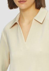 Kremowy sweter z dekoltem w serek i płaskim kołnierzykiem. Wykonany z miękkiego materiału, z prostym przeszyciem i gładką teksturą.