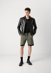 Chaqueta de cuero negra sobre una camiseta negra, combinada con pantalones cortos estampados en verde y negro, calcetines negros y mocasines negros.