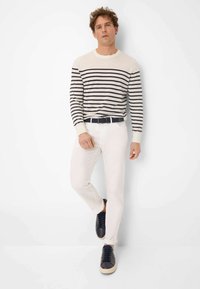 Gebreide trui met crèmekleurige en marineblauwe strepen, gecombineerd met witte slim-fit broek en donkere sneakers. Casual ontwerp en zachte textuur.